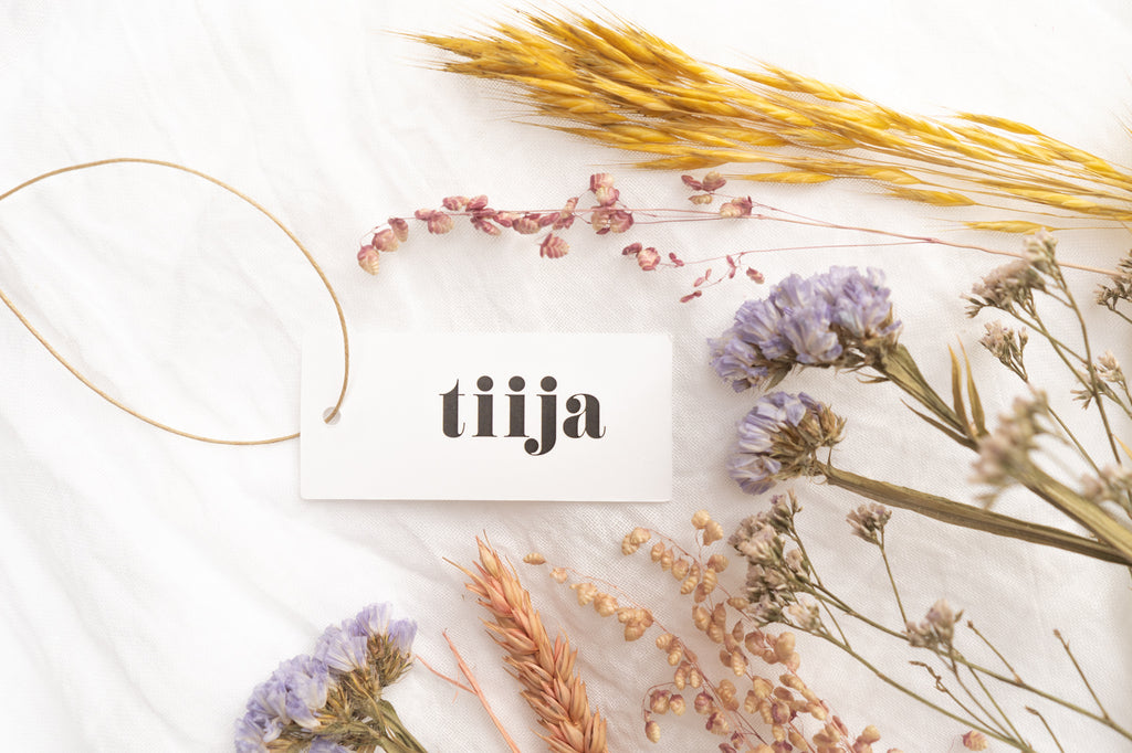 Tiija logo printed on a hangtag, dried flowers arranged around it. tiija is always inspired by nature fair fashion.